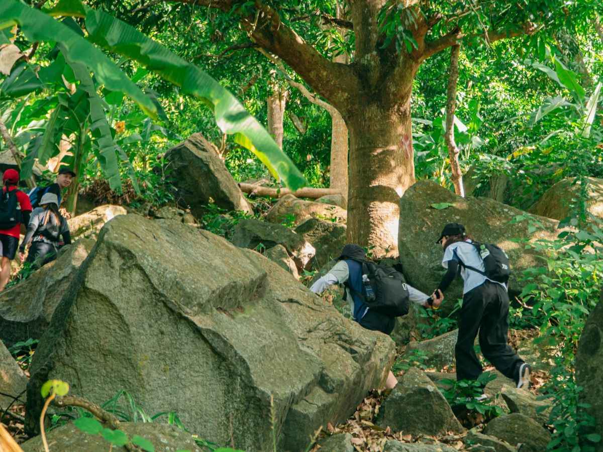 Nhóm du khách trekking qua địa hình đá giữa rừng xanh Núi Bà Đen. 